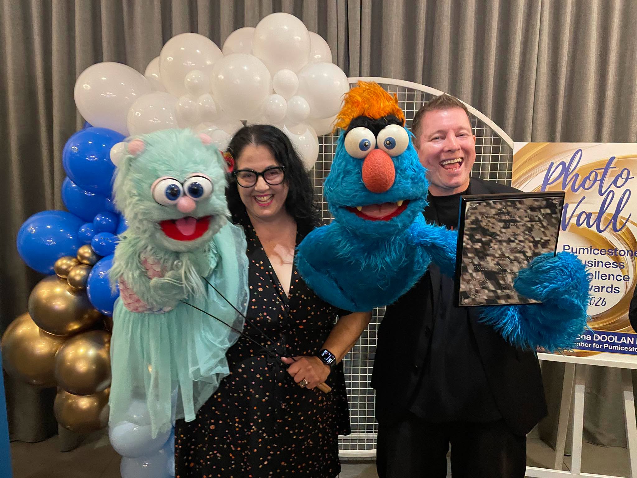 Brett Hansen and Elissa Jenkins with puppet characters Troggg and Marina after winning the Creative Industries Award at the 2026 Pumicestone Business Excellence Awards.